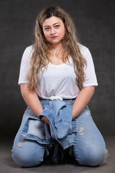 Beautiful fat woman in denim clothes on a gray background. Plus size model girl.