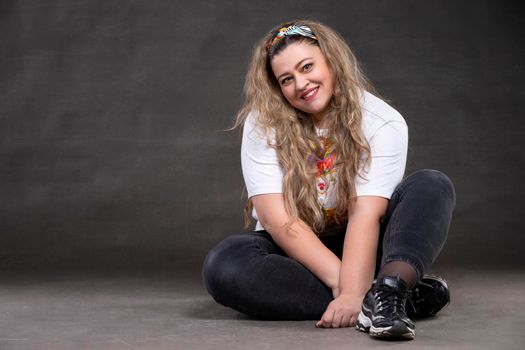 Beautiful fat woman on a gray background looks at the camera and smiles. The girl is a plus size model.