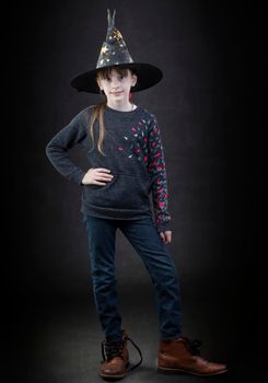 Little girl wearing a witch hat on a dark background.