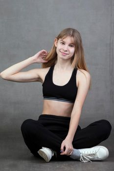 Plain teenage girl in sportswear on a gray background.