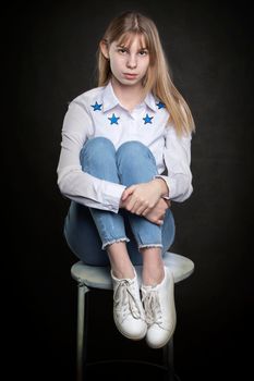 Beautiful teenage girl in jeans and a white shirt is shot against a gray background.