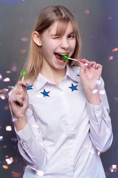 A funny and mischievous teenager girl with a lollipop on a background of multi-colored candy. Girl at a fun party.
