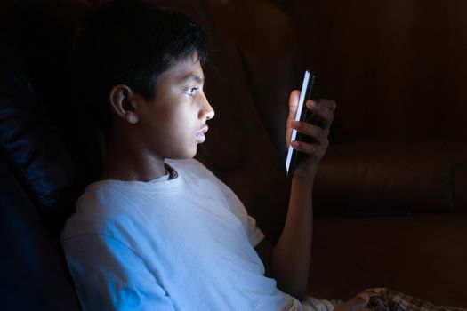 teenage boy sitting on sofa using smart phone at night .