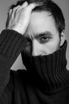 Closeup sexy handsome man wearing warm pullover with high collar and touching hair, looking seductive, flirting at camera, male fashion, vogue concept. black and white, indoor studio shot isolated