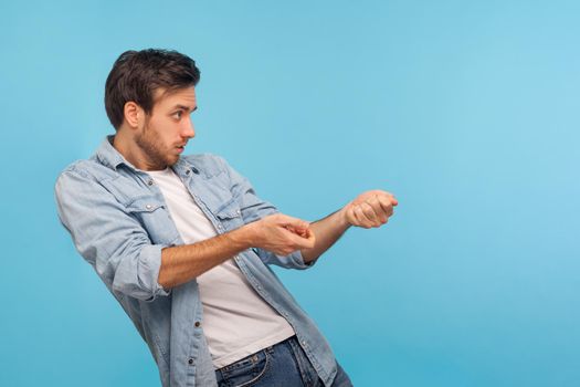 Portrait of hardworking persistent man in worker denim shirt pulling virtual rope, imitating to hold heavy object, striving and making great effort. indoor studio shot isolated on blue background
