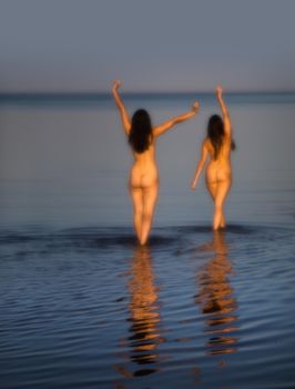 Soft focus image of a beautiful naked girl outdoors enjoying nature. Two young nude women posing on sea background. Sexy naked brunettes enjoying summer time outdoors. View from the back