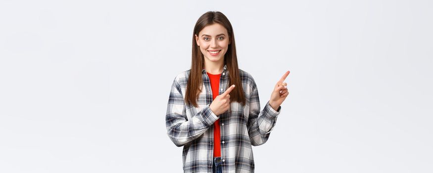 Lifestyle, different emotions, leisure activities concept. Friendly-looking attractive caucasian girl in checked shirt inform about new promos, pointing fingers right and smiling camera.