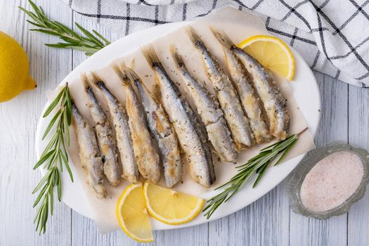 Close-up top view fried capelin on a white porcelain dish with lemon, rosemary and spices. Healthy food concept. Selective focus.