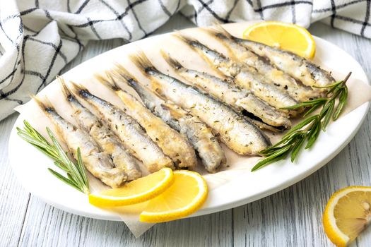 Close-up of fried capelin on a white porcelain dish with lemon, rosemary and spices. Healthy food concept. Selective focus.