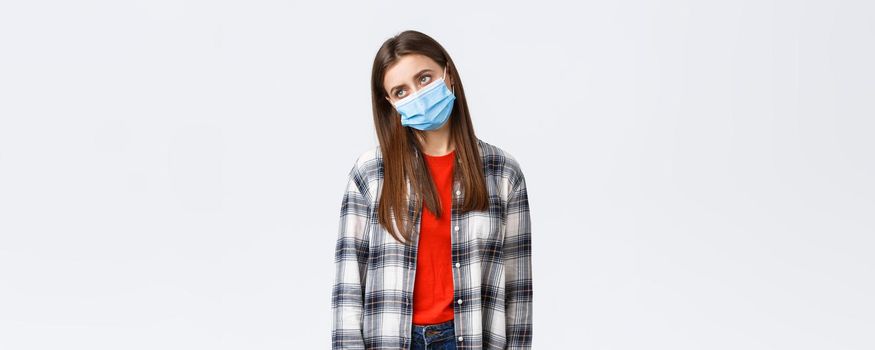 Coronavirus outbreak, leisure on quarantine, social distancing and emotions concept. Gloomy and bored, sad young woman in medical mask, sighing look away reluctant, fed up sit home.