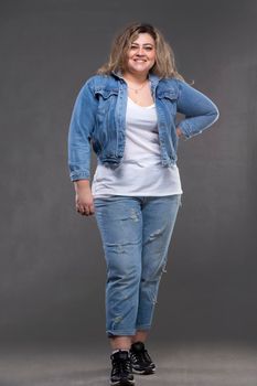 Beautiful plump woman in a denim suit on a gray background.