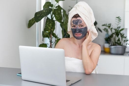 Beautiful young woman working on laptop computer while sitting at the living room with face mask. Beautiful young woman smiling with face mask and looking at laptop screen.