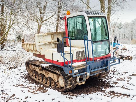 Small Dumper Tracked Truck with Muddy Chassis. The transporter waiting in the snowy forest