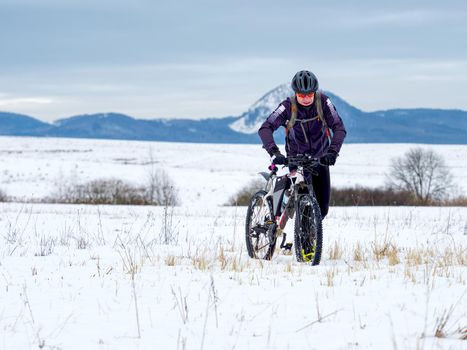 Adult athlete pushes a mountain bike through the snow across a frozen meadow. Hard terrain, the biker can't ride.