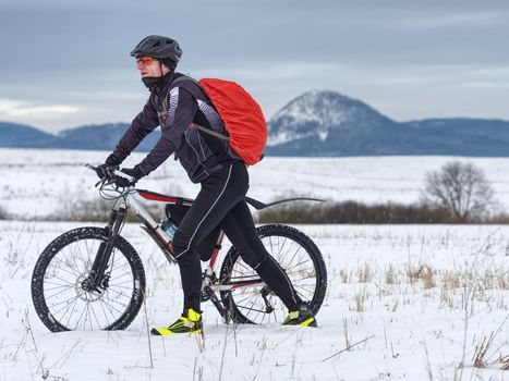 Adult athlete pushes a mountain bike through the snow across a frozen meadow. Hard terrain, the biker can't ride.