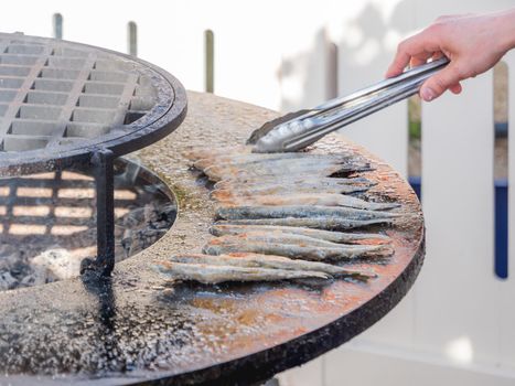 Unrecognizable man is cooking fish on barbeque grill. Fried smelt on cast-iron furnace.
