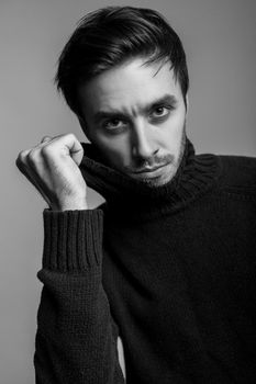 Portrait of sexy handsome man with stylish hairdo wearing warm sweater, pulling sweater collar and looking seductive, flirting at camera, male fashion, vogue concept. black and white, indoor isolated