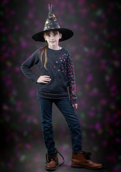 Little girl in a witch's hat on a background with colored spots. A child at the hallowen holiday.