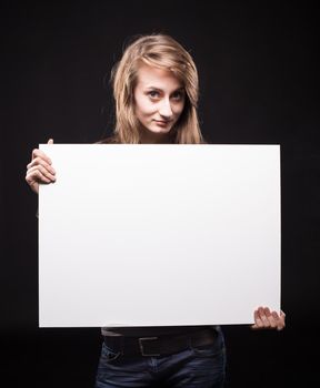 Teenage girl with an empty board for advertising and announcements. Fashion, portrait and people concept. Portrait of a young emotional woman on a dark background