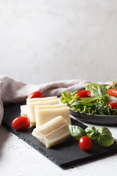 A piece of fresh sliced halloumi on a slate board with cherry tomatoes and spinach leaves. Preparing to cook cheese on the grill. Copy space.
