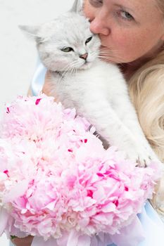 the hostess hugs a cute gray kitten with green eyes of the Scottish breed against the background of pink peonies and a blue dress of the bride. High quality photo