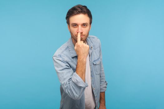 Don't lie to me. Portrait of man in worker denim shirt touching nose, showing liar gesture, angry about falsehood, outright deception, fake news. indoor studio shot isolated on blue background