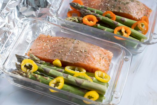 raw red salmon with salt and spices with green asparagus and paprika in a baking dish covered with foil. High quality photo