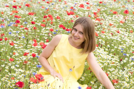 a beautiful young blonde woman in a yellow dress stands among a flowering field of poppies, daisies, cornflowers and laughs. High quality photo