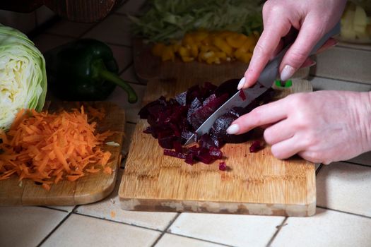 a woman cuts beets in the kitchen against the background of fresh vegetables, ingredients for step by step cooking soup. High quality photo