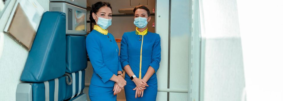 Women stewardesses wearing protective face masks and air hostess uniform while standing near aircraft door