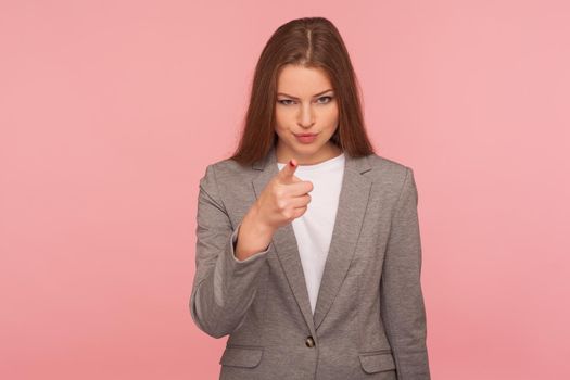 Hey you. Portrait of strict displeased young woman in business suit making choice with indicating finger, looking bossy and dissatisfied, showing guilty. studio shot isolated on pink background