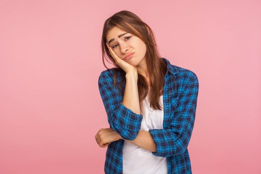 Portrait of bored lazy girl in checkered shirt leaning on hand and looking at camera with disinterest, listening to boring story, disappointed with result. studio shot isolated on pink background