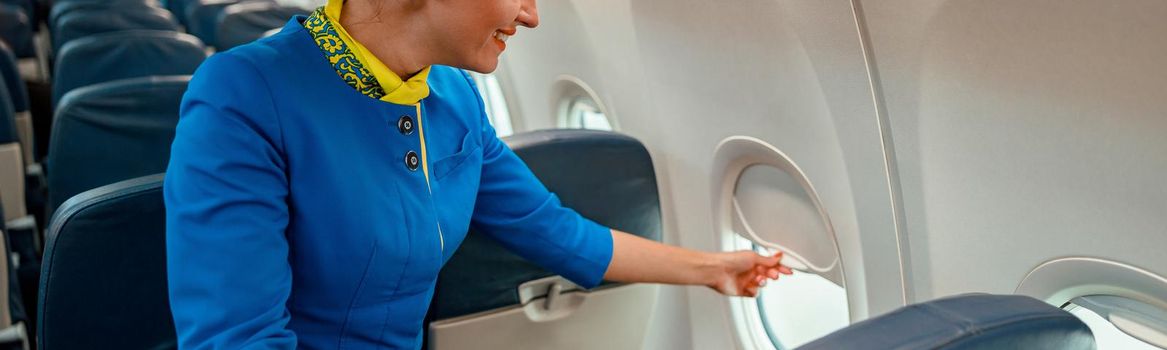 Cheerful flight attendant or air hostess closing window in commercial passenger aircraft