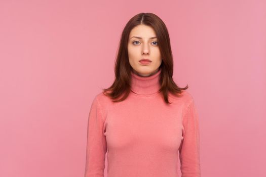 Portrait of serious self assured brunette woman looking at camera with confidence, sensuality and femininity. Indoor studio shot isolated on pink background