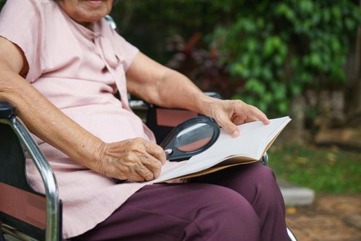 Elderly woman using a magnifying glass to read on wheelchair.