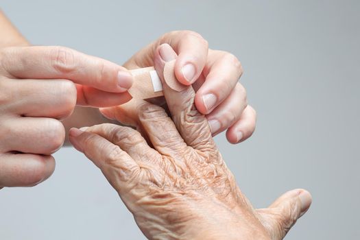 Nurse putting adhesive bandage on elderly woman hand