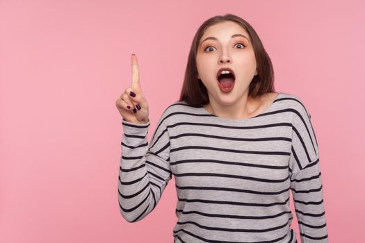 I know answer. Portrait of inspired woman in striped sweatshirt pointing finger up and having good idea, looking amazed surprised by suddenly invented clever solution. indoor studio shot isolated