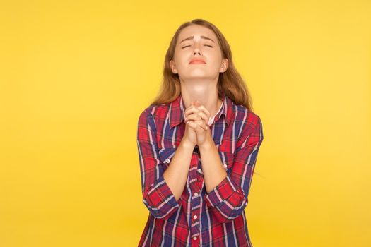 Please I'm begging. Portrait of despaired ginger girl in shirt keeping arms in prayer gesture and holding up head, appealing to god with imploring expression. studio shot isolated on yellow background