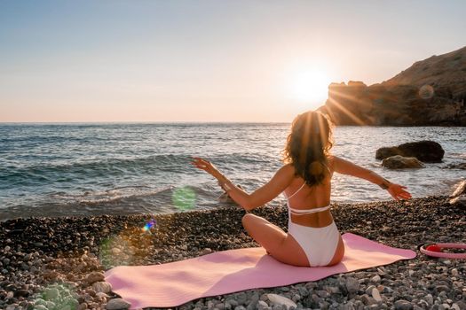 Young woman in swimsuit with long hair practicing stretching outdoors on yoga mat by the sea on a sunny day. Women's yoga fitness pilates routine. Healthy lifestyle, harmony and meditation concept.