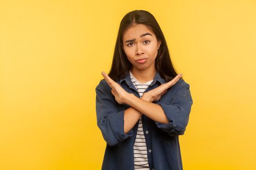 No way, this is finish. Portrait of dissatisfied girl in denim shirt gesturing stop, x sign with crossed hands, way prohibited, warning of troubles. indoor studio shot isolated on yellow background