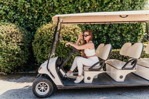 A middle-aged woman is driving a car for transporting tourists. Electric car, Tourist bus. Car for transporting people around the hotel, park, golf club.