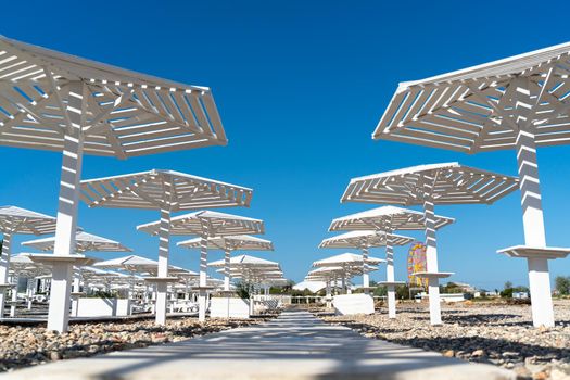 Rows of wooden umbrellas from the sun on the seashore in the morning. Wooden paths on the sand between umbrellas. Beach holiday at the resort