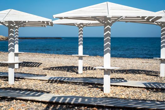 Rows of wooden umbrellas from the sun on the seashore in the morning. Wooden paths on the sand between umbrellas. Beach holiday at the resort