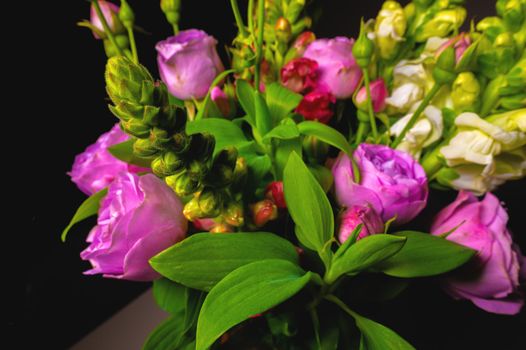 Fresh mixed flower bouquet on black background. Green branches with rich peony roses. Dark floral background.