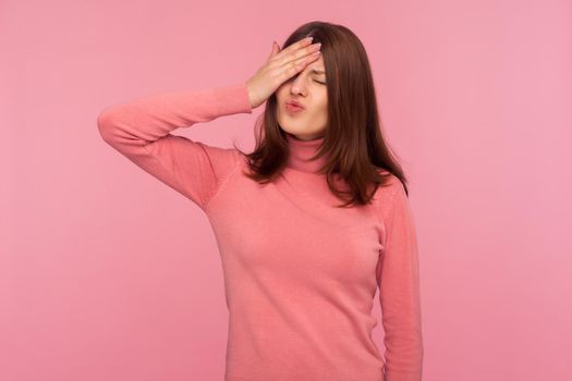 Frustrated disappointed brunette woman making facepalm gesture, shocked, ashamed with lose, failure. Indoor studio shot isolated on pink background