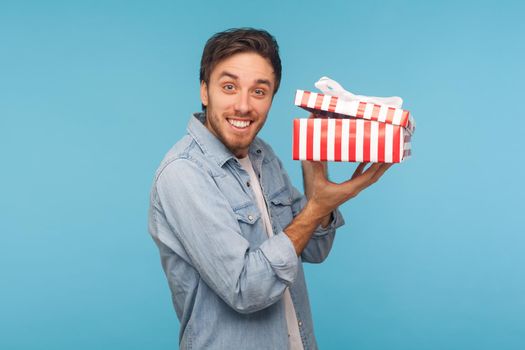 Portrait of excited man in denim shirt holding opened gift box and looking at camera with joyful smile, unpacking present, satisfied with awesome birthday surprise. indoor studio shot, isolated