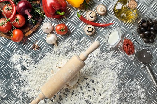 Ingredients and dough for making pizzas with an overhead view on freshly mixed mounds of pastry, a jar of olive oil and pot of tomato sauce, overhead view on metal background. Top view. Flat lay. Still life