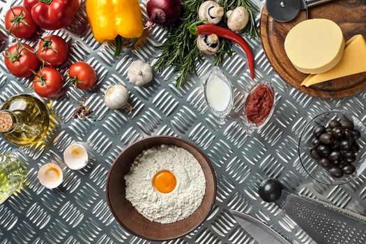Ingredients and dough for making pizzas with an overhead view on freshly mixed mounds of pastry, a jar of olive oil and pot of tomato sauce, overhead view on metal background. Top view. Flat lay. Still life