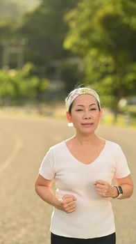 Active mature woman jogging at the park in evening. Healthy lifestyle and fitness concept.