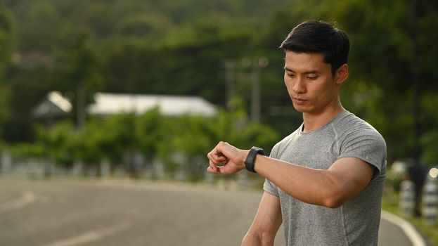 Athletic man resting and checking his heart rate data on smartwatch during morning workout. Sport and healthy lifestyle concept.